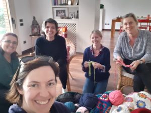 A group of 5 women from IWA Modena in a room with their samples of crochet and balls of yarn and crochet items in the middle
