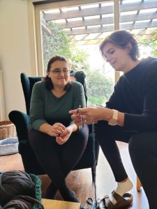 One woman showing another woman a crochet technique while sat in an armchair