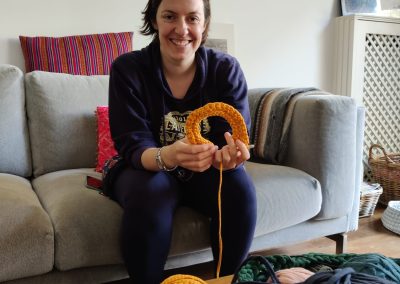 Kelly holding a crochet sample sat on a sofa with yarn and crochet in front at an IWAM Creatives event