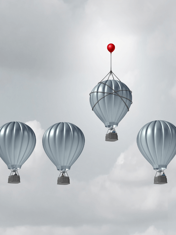 Das Bild zeigt 4 Heißluftballons, von denen einer mit einem zusätzlichen Luftballon weiter hoch gezogen wird