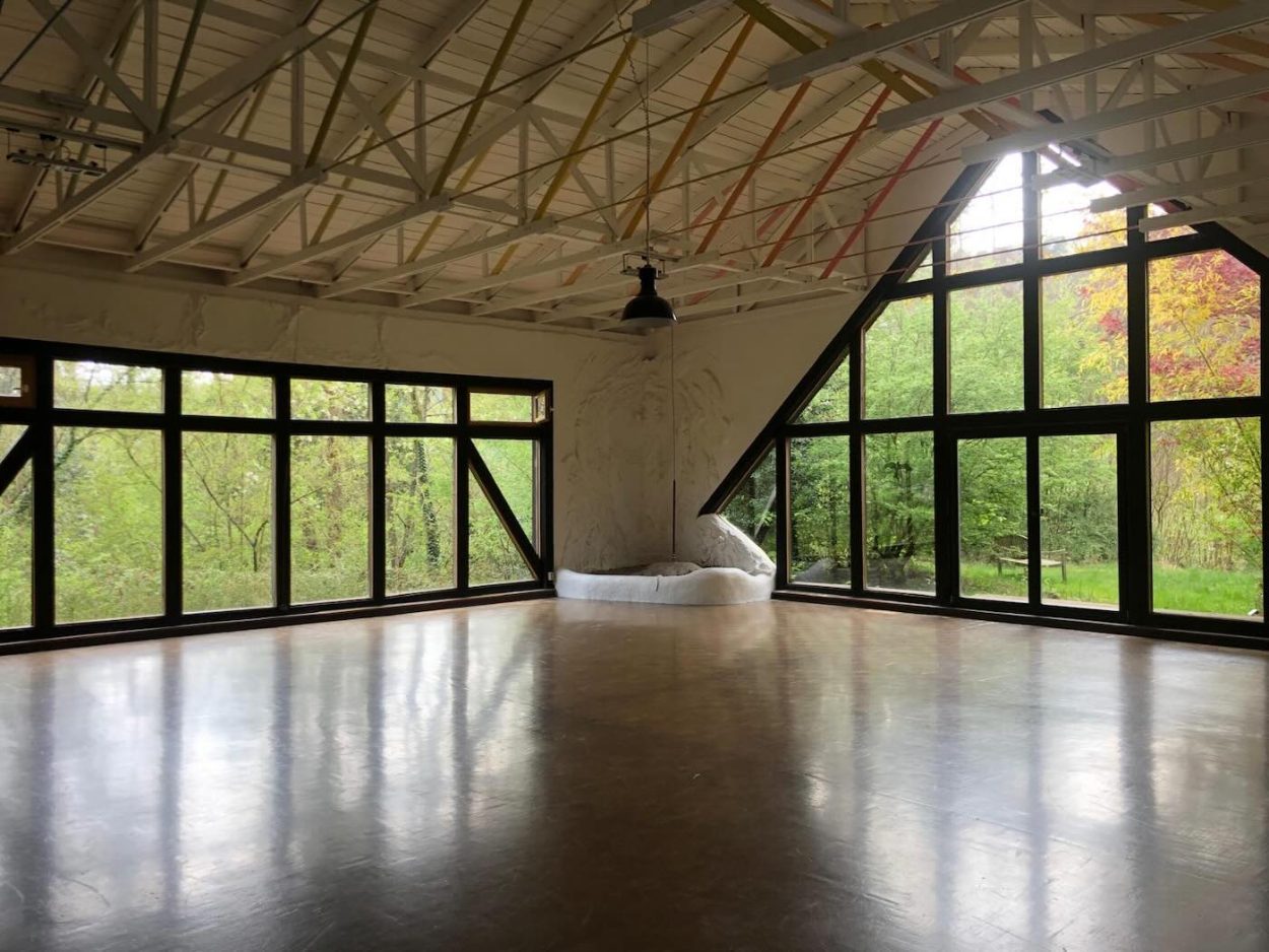 Dieser großzügige Yogaraum in der Grube Louise im Westerwald bietet mit seinen hohen Decken, der offenen Architektur und den bodentiefen Fenstern einen idealen Rahmen für tiefgehende Retreat-Erfahrungen. Das Bild zeigt den Raum in seiner ganzen Weite, mit Blick auf das satte Frühlings- oder Herbstgrün des Waldes. Perfekt für Vinyasa, Yin Yoga, Meditation, Mantrasingen oder Sharing Circles im Rahmen des Yoga Retreats mit JayJay & Hannah. Hier entsteht eine kraftvolle Verbindung von innerem Prozess und äußerer Natur – ein Ort der Klarheit, des Friedens und der Transformation.