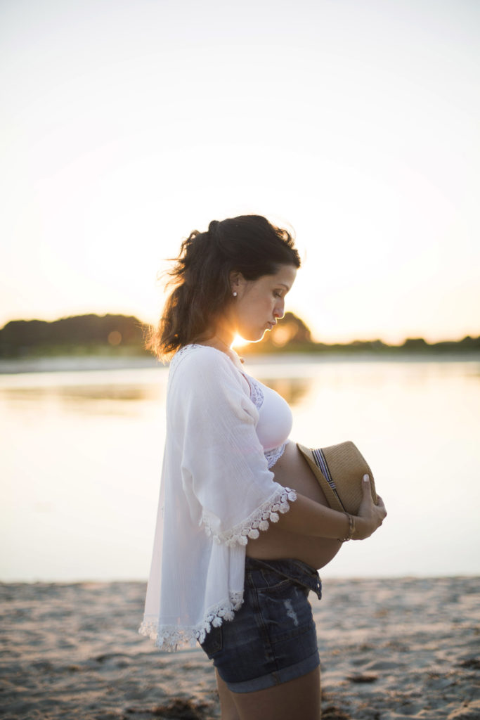 Femme enceinte poser un chapeau en paille sur son ventre sur la plage pendant le coucher de soleil