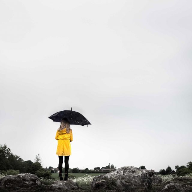 En tjej med gul regnjacka står med ett paraply gjort av stjärnor i bister miljö