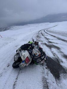 Lange kurvige schneebedeckte Stra&szlig;e durch wei&szlig;e Felder mit seitlich liegender bepackter wei&szlig;er Vespa