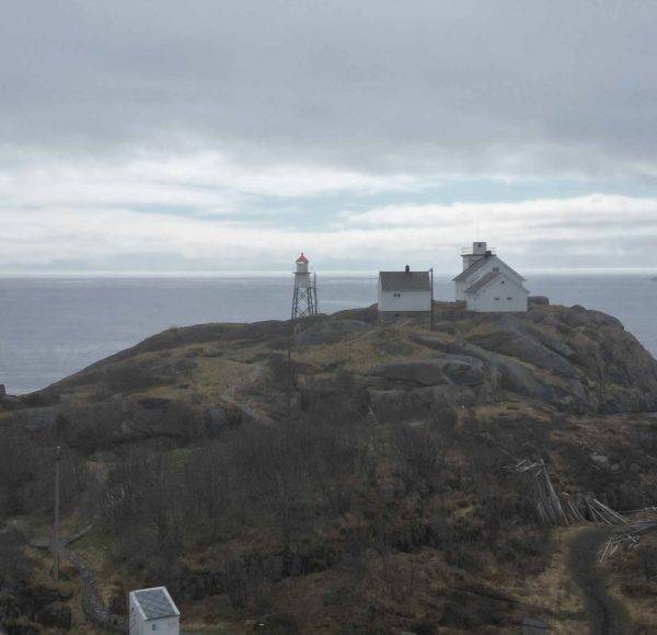 Ein Leuchtturm und Gebäude stehen auf einer felsigen Klippe mit Blick auf das Meer unter bewölktem Himmel.