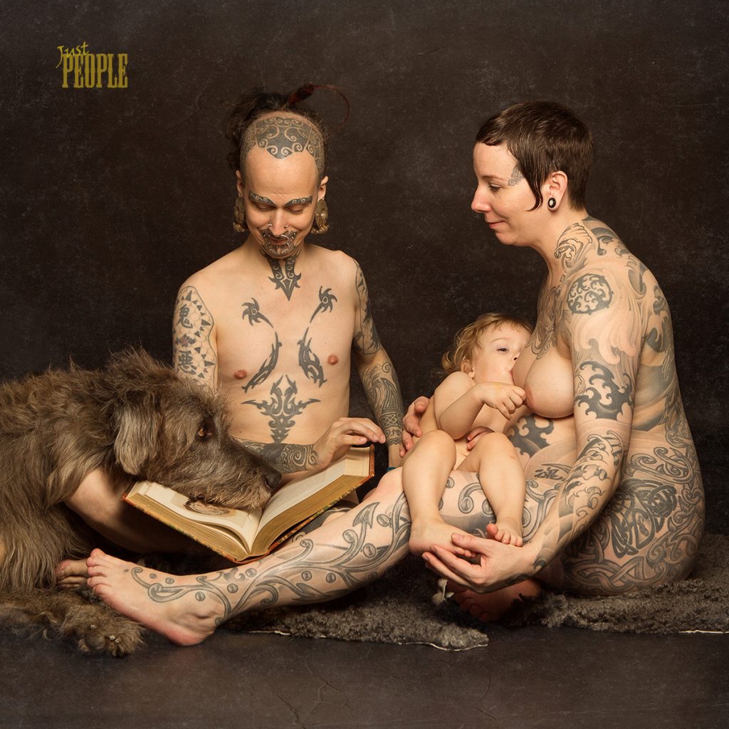 Family sitting reading a book. Mother is breastfeeding and the dog is laying his head on the book. Family is tattoed