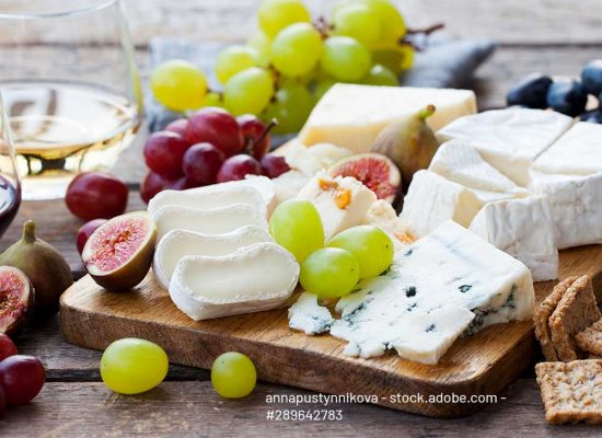 Cheese and fruits assortment on cutting board with red, white wine on wooden background