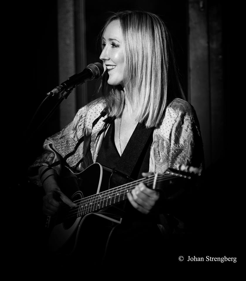 Kajsa Larsson - Trubadur på fest i Huddinge - håller i en gitarr, ler