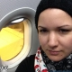 Eine junge Frau mit Beanie Mütze und Aspen Vista Halskrause sitzt in einem Flugzeug