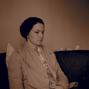 Eine junge Frau mit Beanie Mütze, den Blick gesenkt auf einem Sofa. Sie trägt einen grauen Sweater und blickt auf ihren Computer