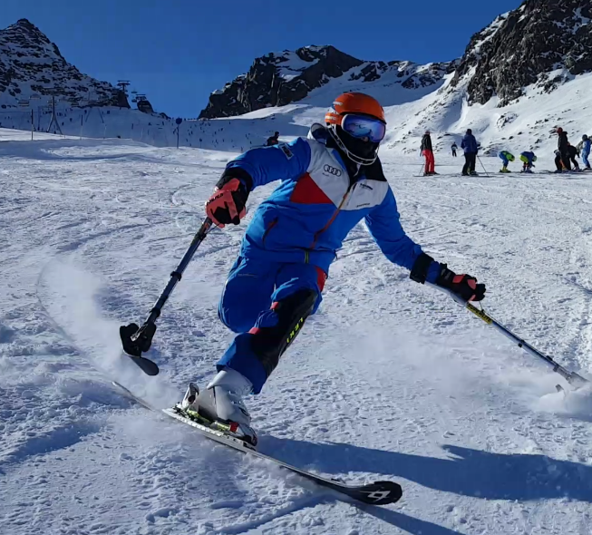 Christoph Glötzner rast auf einem Bein den Berg hinab. Er trägt einen blauen Skianzug, einen roten Helm und einen Schal der sein Gesicht verdeckt.