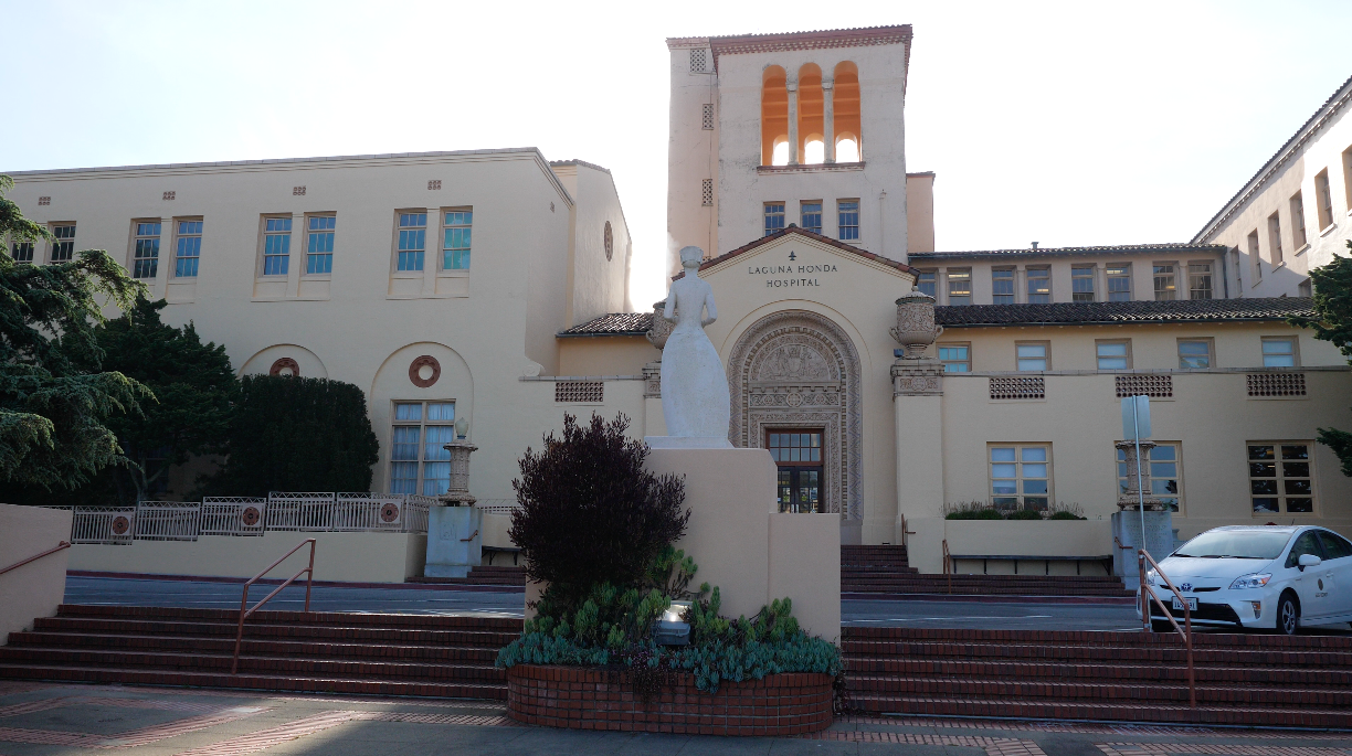 Old Building of the Laguna Honda Hospital in San Francisco with a statue in the foreground.