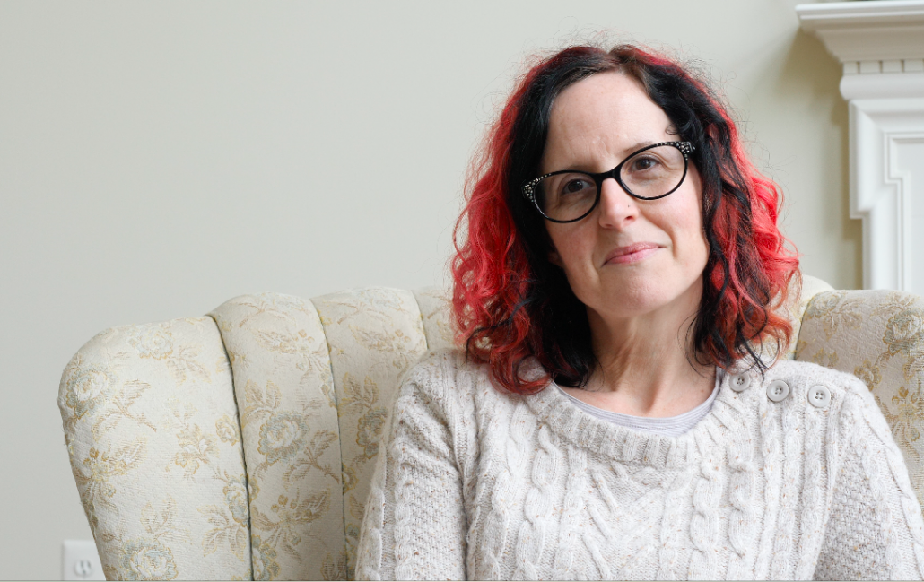 Mid-size front shot of a woman with shoulder-long black and red hair and black, sparkly glasses.