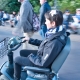 Karina, eine Frau mit kurzen, braunen Haaren sitzt in einem elektronischen Scooter und fährt neben zwei Männern auf einer breiten Straße entlang