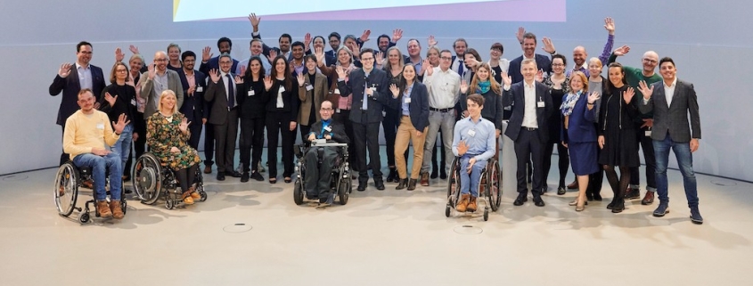 Gruppenfoto mit diversen Menschen in Anzügen und schicker Kleidung, die alle winken