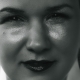 A super close up of a woman's face. She is smiling slightly and wears huge silver earrings and red lipstick.