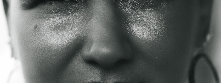 A super close up of a woman's face. She is smiling slightly and wears huge silver earrings and red lipstick.