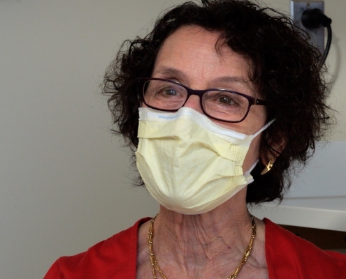 Dr. Wolf, a woman with short, curly brown hair, black glasses and a yellow face mask.