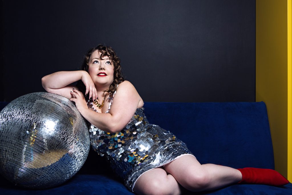 Here I am in my shiny silver sequinned outfit sitting on a blue couch leaning on the giant silver disco ball looking up towards the sky
