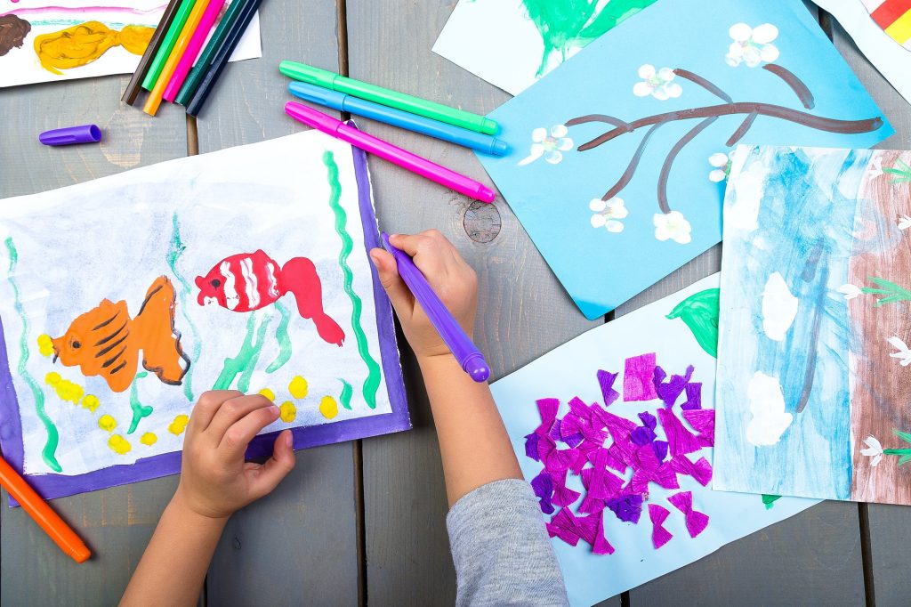 Child drawing. Top view of child hands with pencil painting picture on paper. Kid drawings.