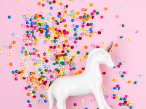 Flat lay with white unicorn and colorful glitter over the pink background. Magic surreal, fairy tale