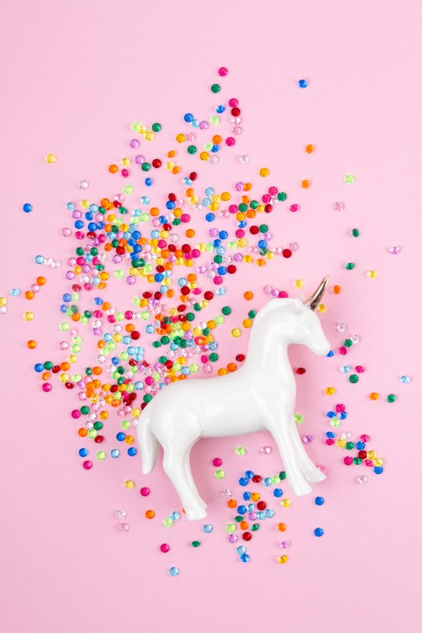 Flat lay with white unicorn and colorful glitter over the pink background. Magic surreal, fairy tale