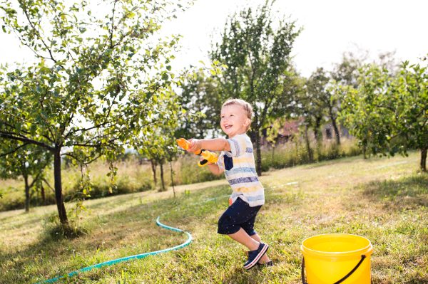 Little boy with water gun splashing somebody, sunny summer garde