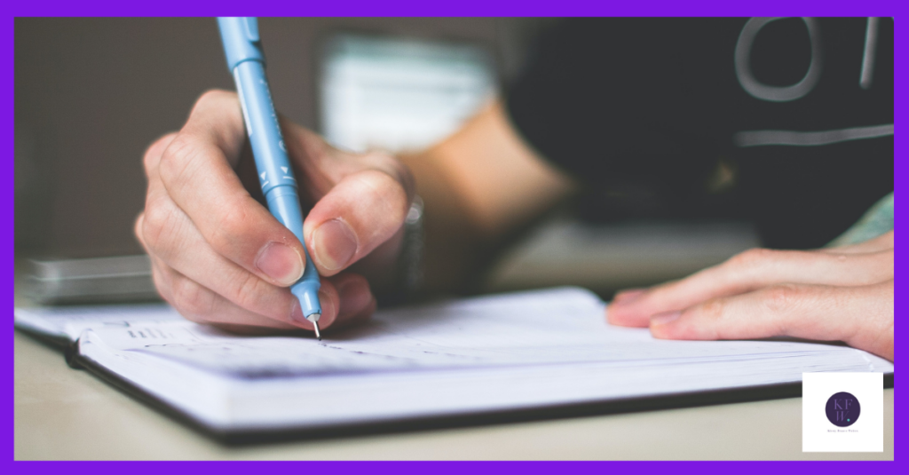 The image shows a woman in a black t-shirt writing on a notepad, probably wondering if her grammar is OK.