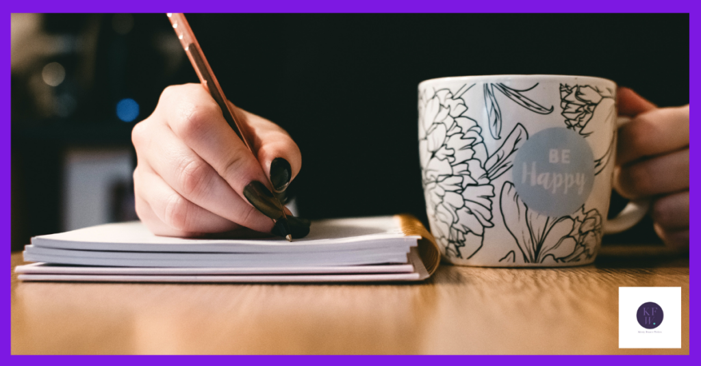 Image shows a woman with black fingernails and a 'be happy' mug using a pen to write marketing content in her notebook.