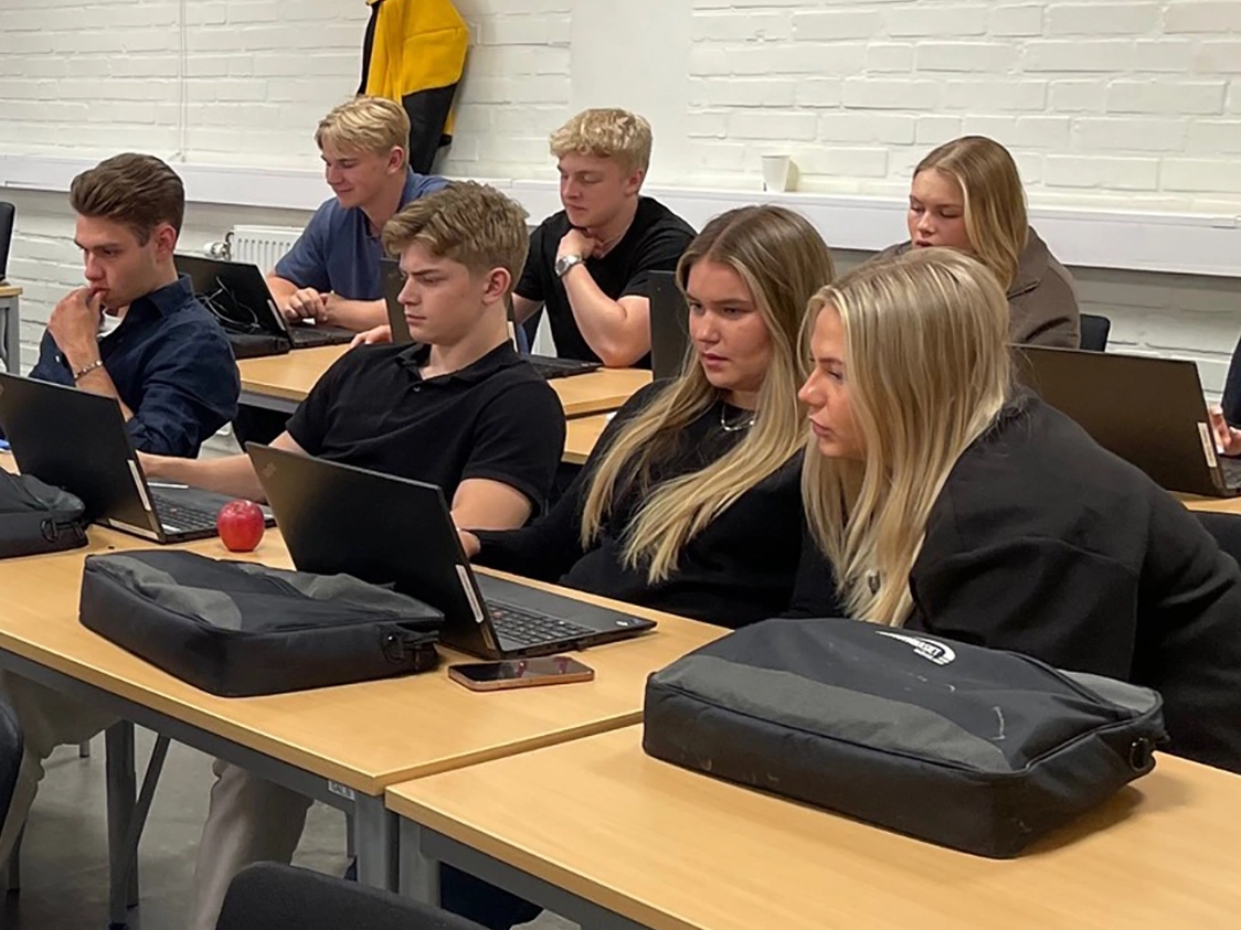 Grupp av studenter i ett klassrum som arbetar med laptops, fokus på samarbete och inlärning.