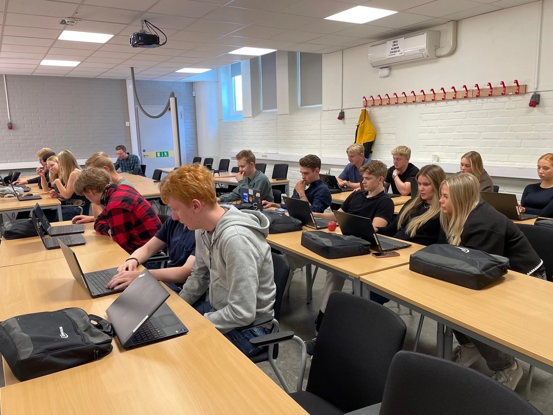 Grupp av studenter i ett klassrum som arbetar med laptops, fokus på samarbete och inlärning och spelar klimatspelet. 