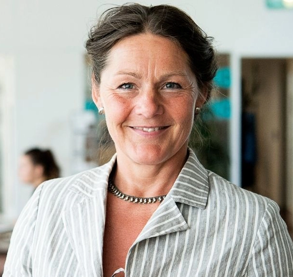 Helle Gerbild, Smilende kvinde i 50erne med langt mørkt hår stående foran farvestrålende maleri