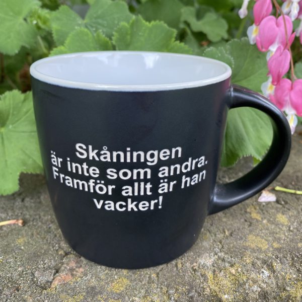 Svart mugg med sandblästrad text: Skåningen är inte som andra. Framför allt är han vacker!