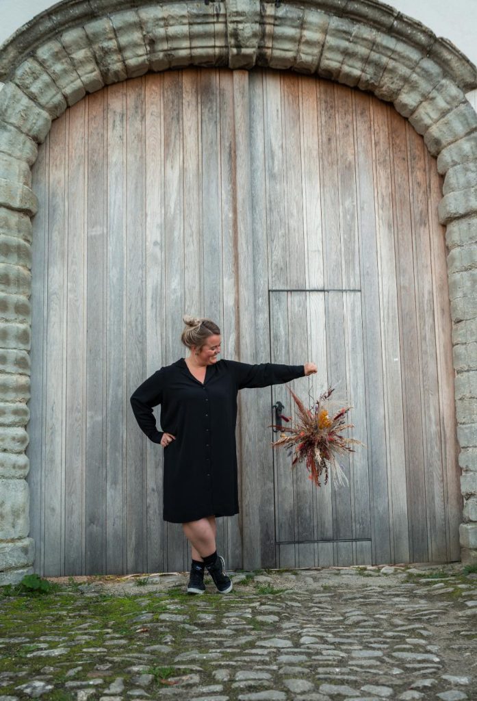 Dorien van Kontent voor een houten poort met een bloemenwolk in de hand