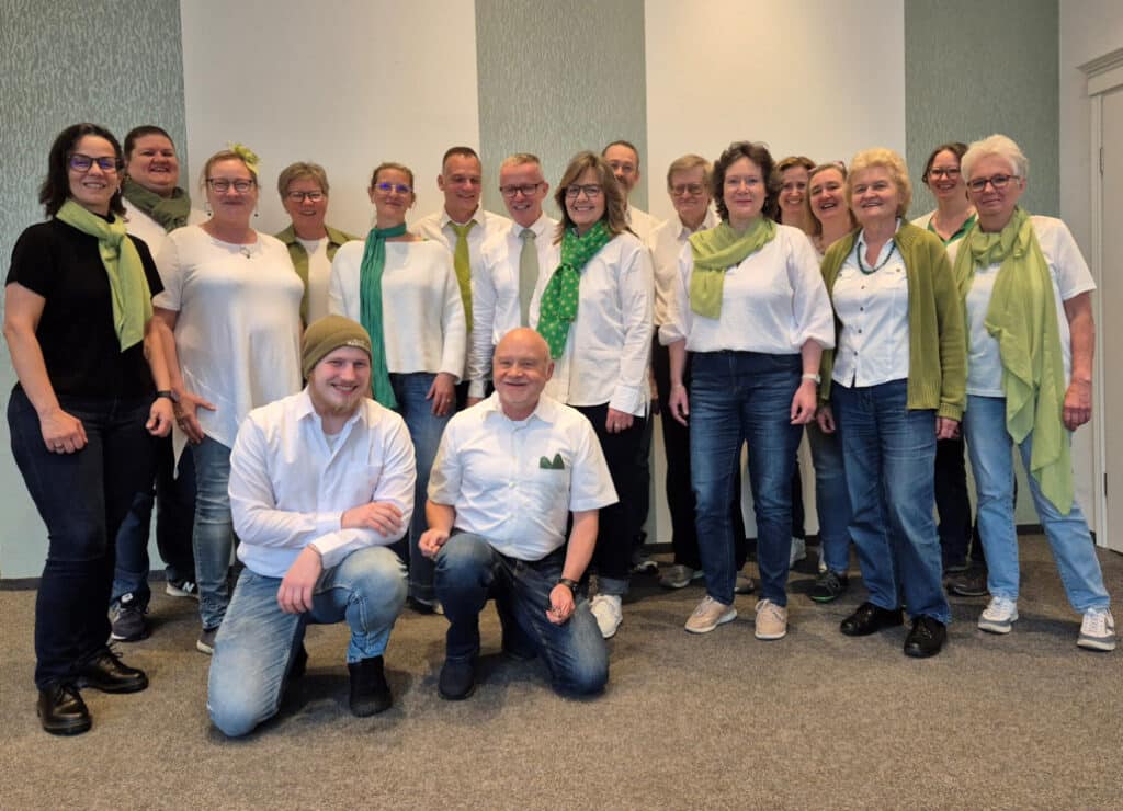 Eine Gruppe Menschen steht im Halbkreis, zwei Männer hocken davor.