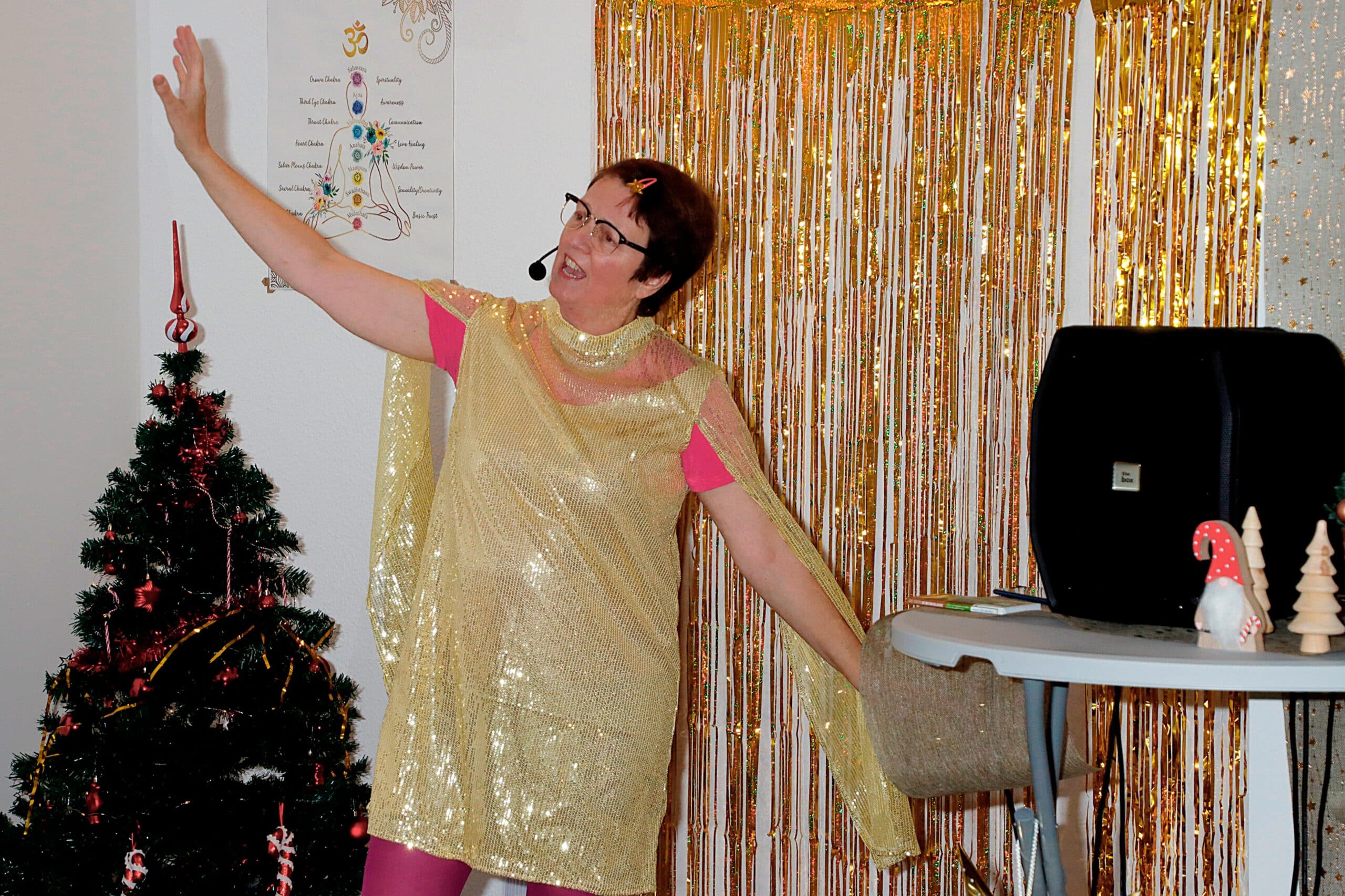 Kulturadvent 2024-12-11 Wichtel im Tal Studio1 ©OMK Media Dörte aus Heckinghausen singt im goldenen Kleid in schwungvoller Pose, im Hintergrund ein Weihnachtsbaum und -deko
