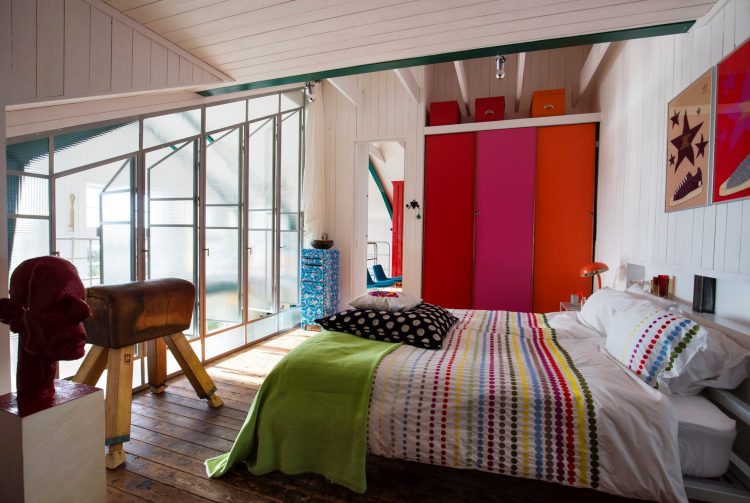 väst rum på Lådfabriken -creative seaside accommodation- med dubbelsäng, fönstrar, konst på väggen, färgstark förvaring i bakgrunden