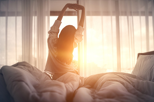 en kvinna i sängen stretchar i motljus 