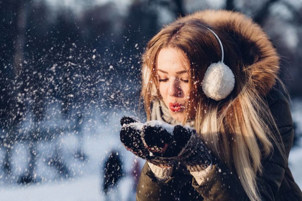 Prepararse para el invierno en Alemania - Imagen ilustrativa chica requetemona con ropa de abrigo en la nieve soplando unos copos de sus manos