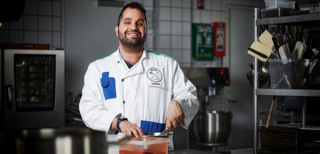 The founder of Madsynet (Food Vision), Mohammed Alsaadi, is standing in a kitchen cooking while smiling at the camera.