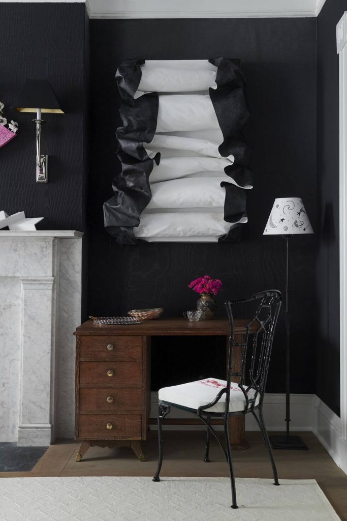McCauley transforms a corner with inky dark walls, showcasing a black and white sculptural piece above a desk. 