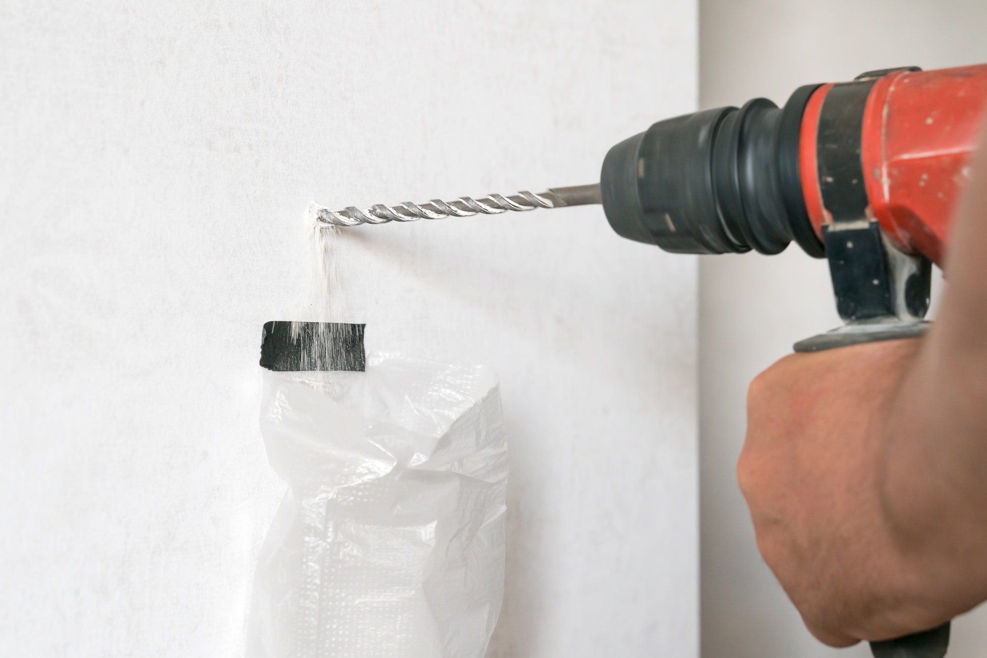 Close-up male hands holding an electric hammer drill and drilling a hole in the wall