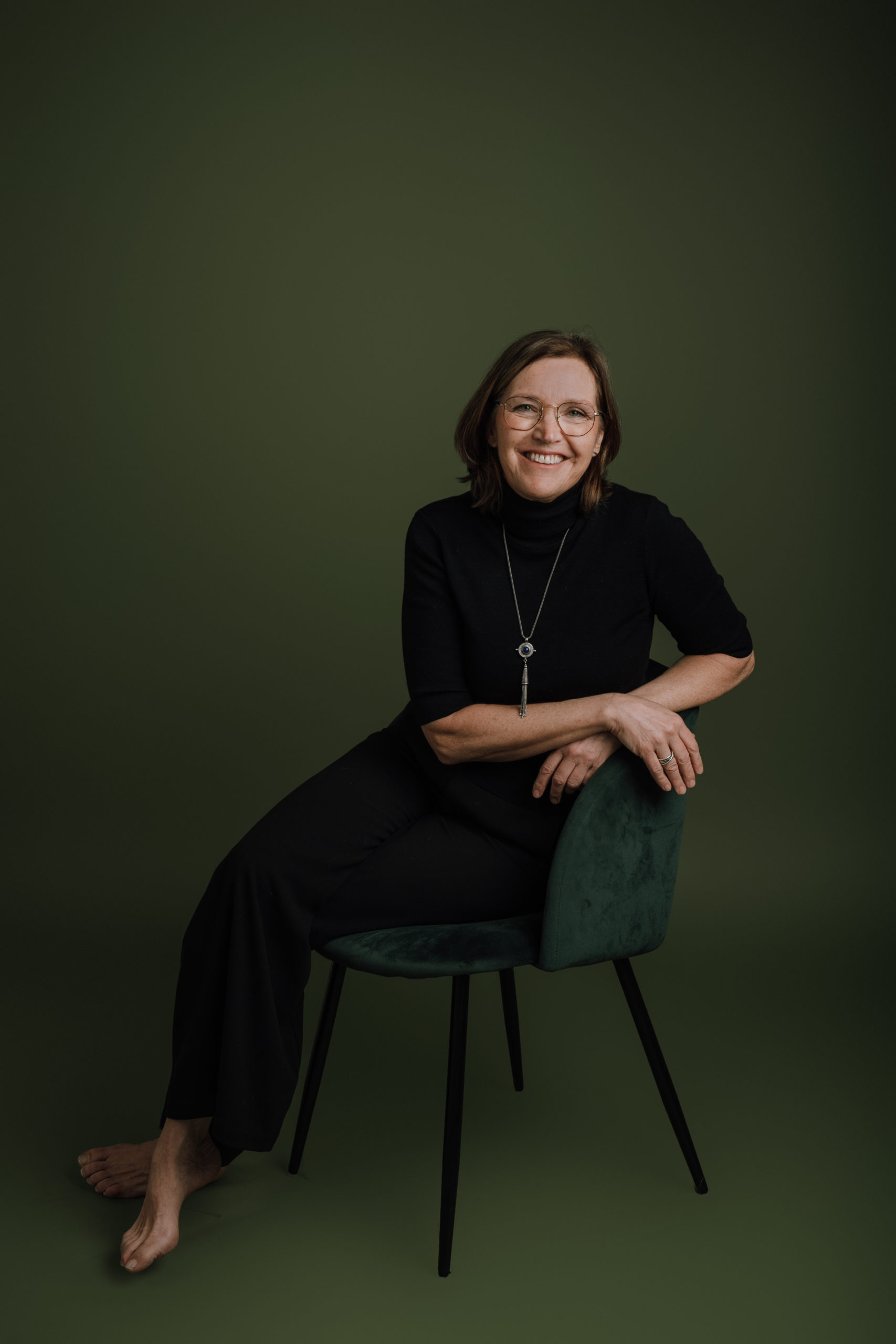 Dette er et bilde av vetrinær Helen Øvregaard. Hun sitte på en grønn stol på en grønn bakgrunn. Hun har beina i kors, lener seg til armlenet og smiler til kamera.