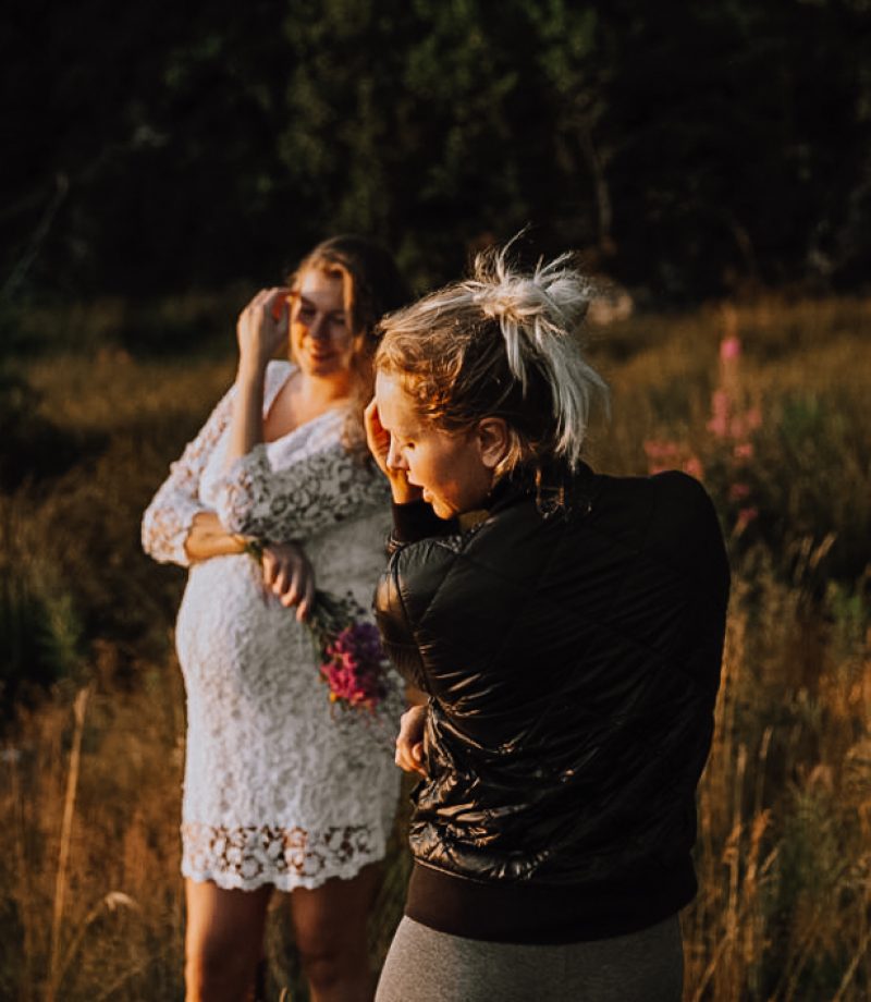 Fotograf Lene Fossdal viser en gravid kunde hvordan hun skal posere. De står ute i en eng i solnedgang.