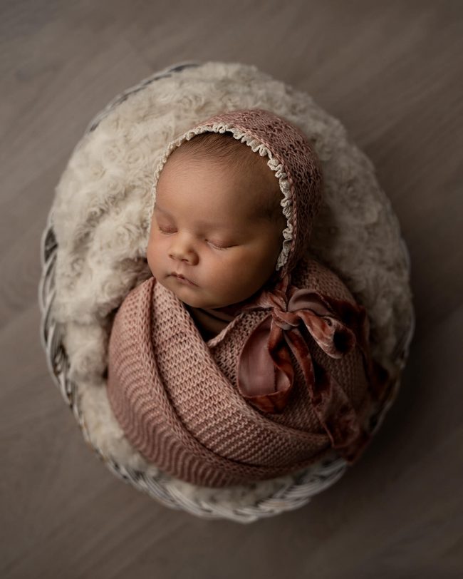 En nyfødt baby wrappet i rosa ligger i en oval kurv.