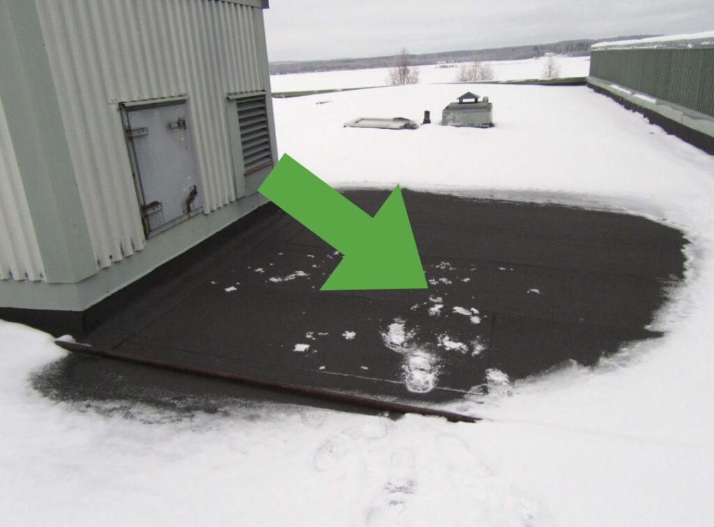 Snötäckt tak med stor grön pil på yta utan snö