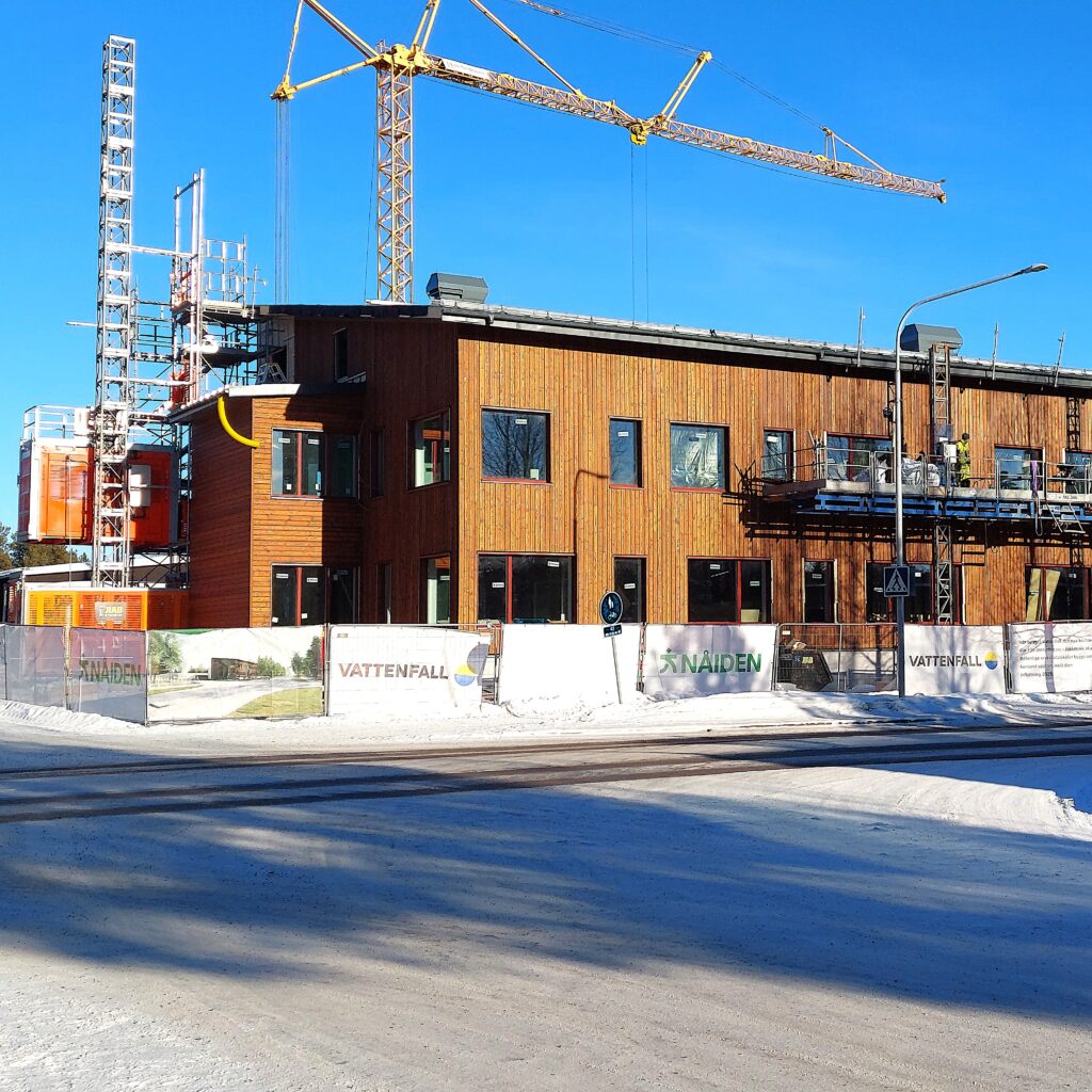 Bygge av byggnad i träfasad med lyftkranar och byggnadshissar