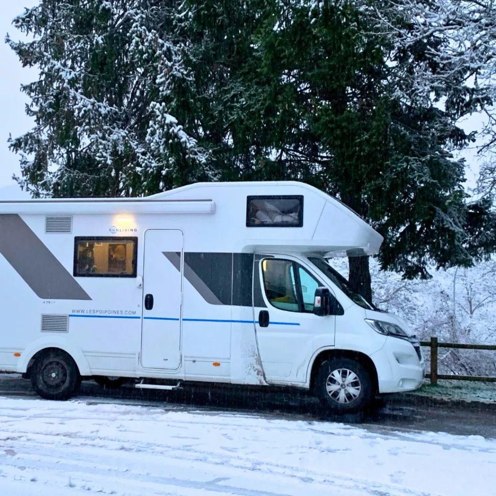 Camping-car stationné dans un paysage hivernal enneigé avec des montagnes en arrière-plan