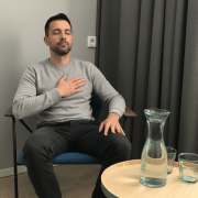 man_zit_in_stoel_therapeutisch_lichaamsbewust Man ervaart lichaamsbewustzijn tijdens moment van zelfreflectie in therapeutische setting