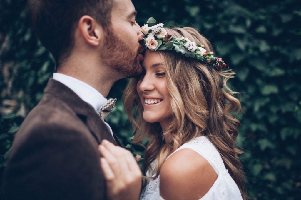 Ein Bräutigam küsst seine grinsende Frau auf die Stirn